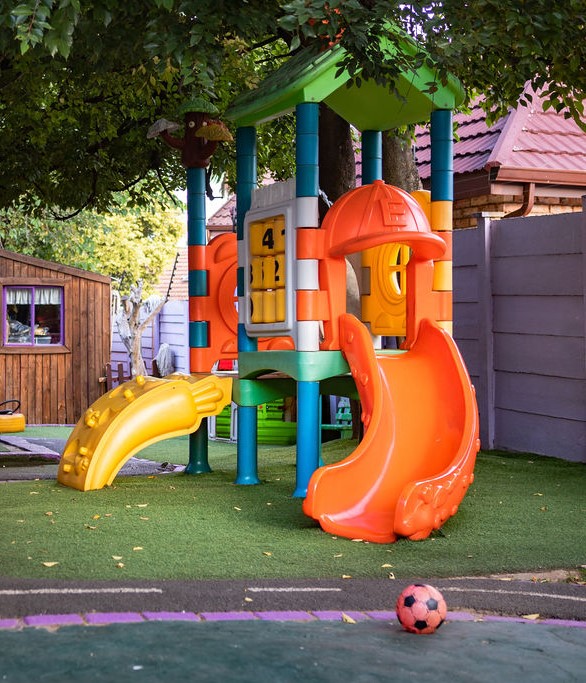Colourful low-level plastic jungle gym with slide on soft turf